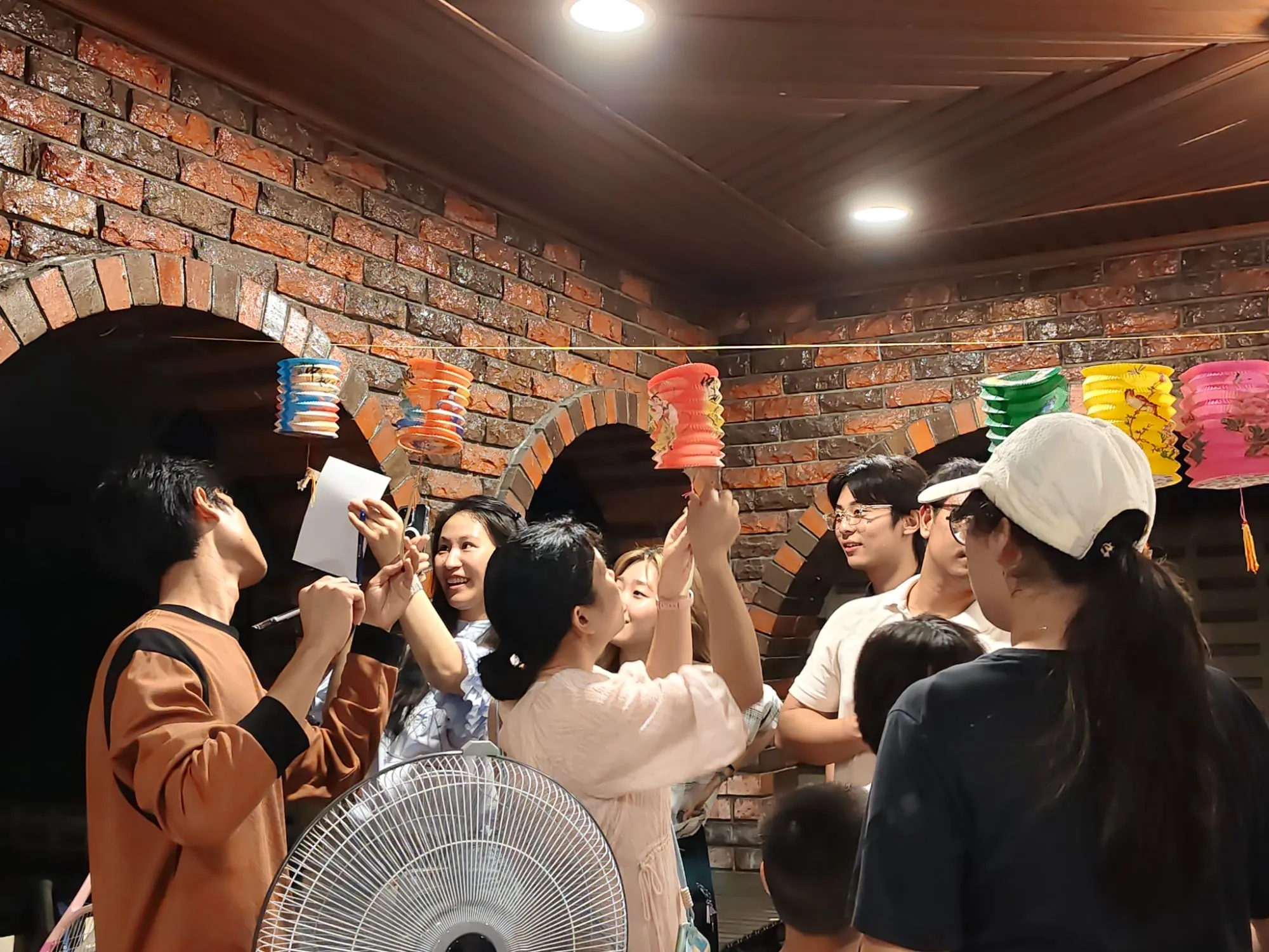 International students laughing as they reach up to read riddles hanging from paper lanterns at a Mid-Autumn celebration