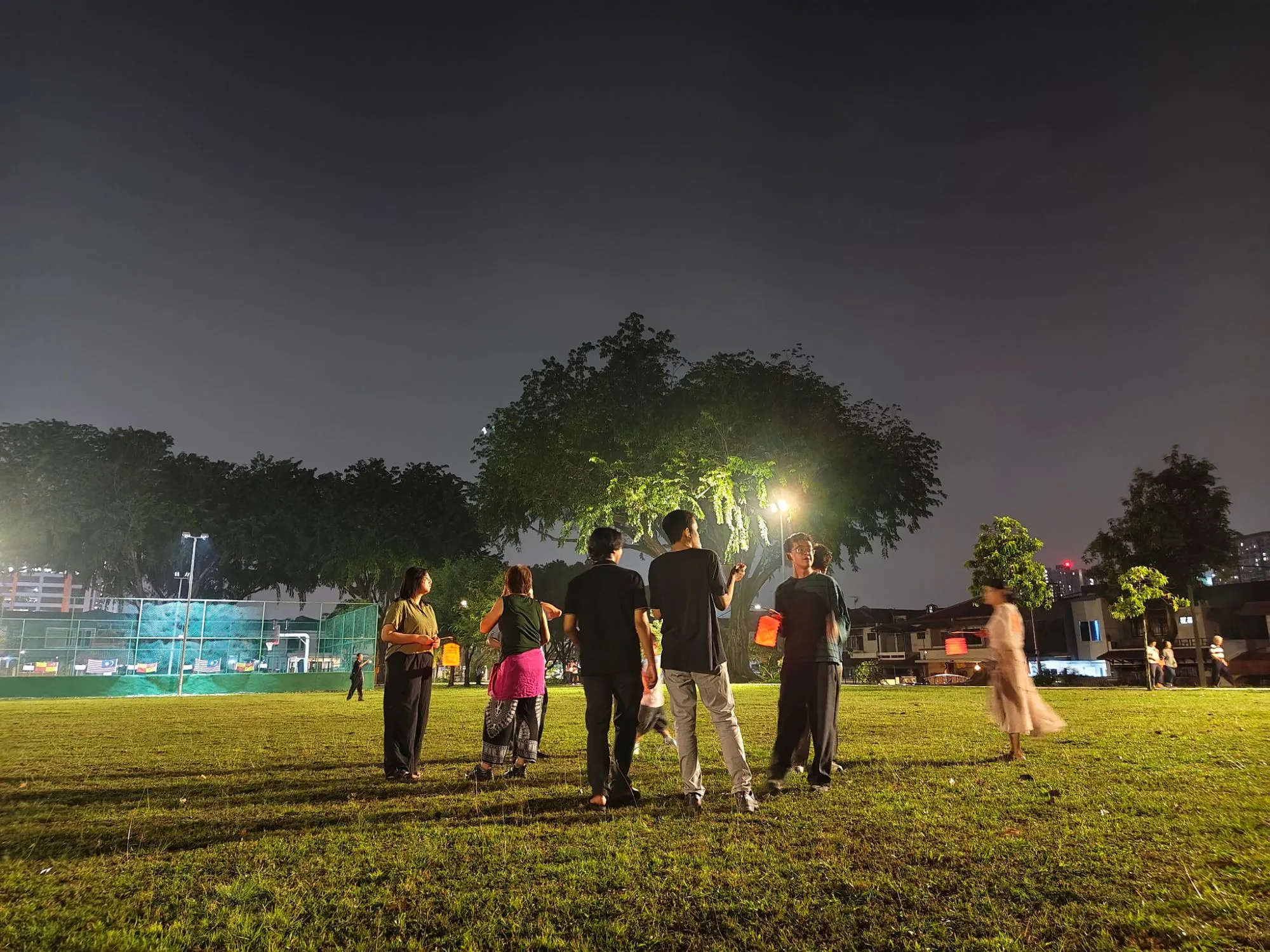 Students carrying lit paper lanterns across a grassy field at night