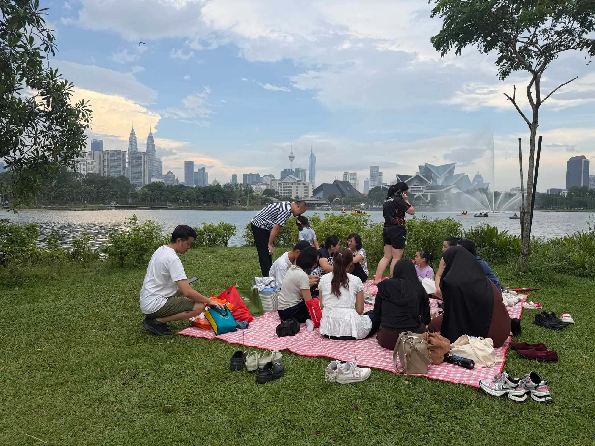 Students and volunteers having a picnic by a lake, with the Kuala Lumpur skyline behind them