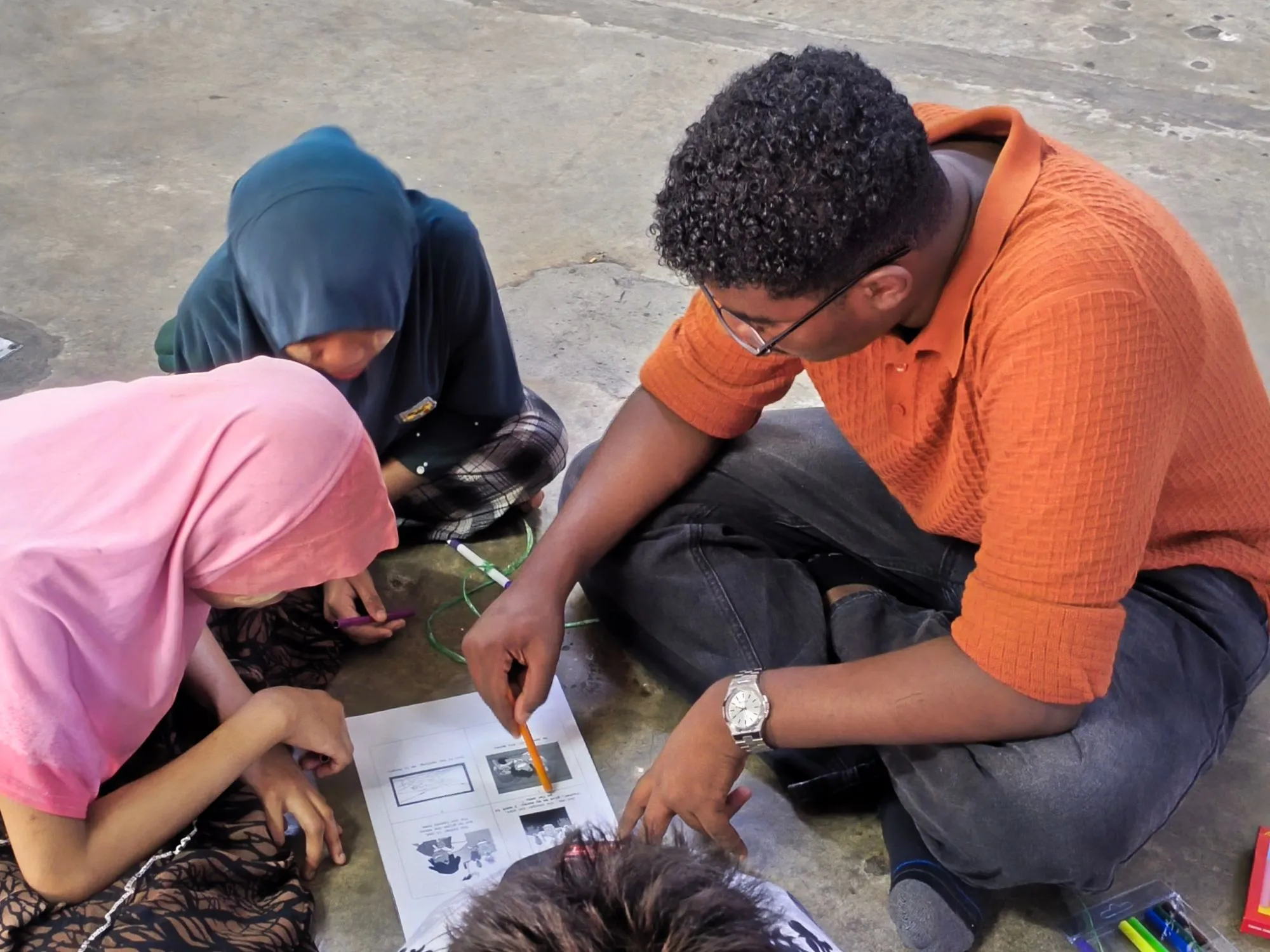 A student volunteer helping two children with a picture worksheet